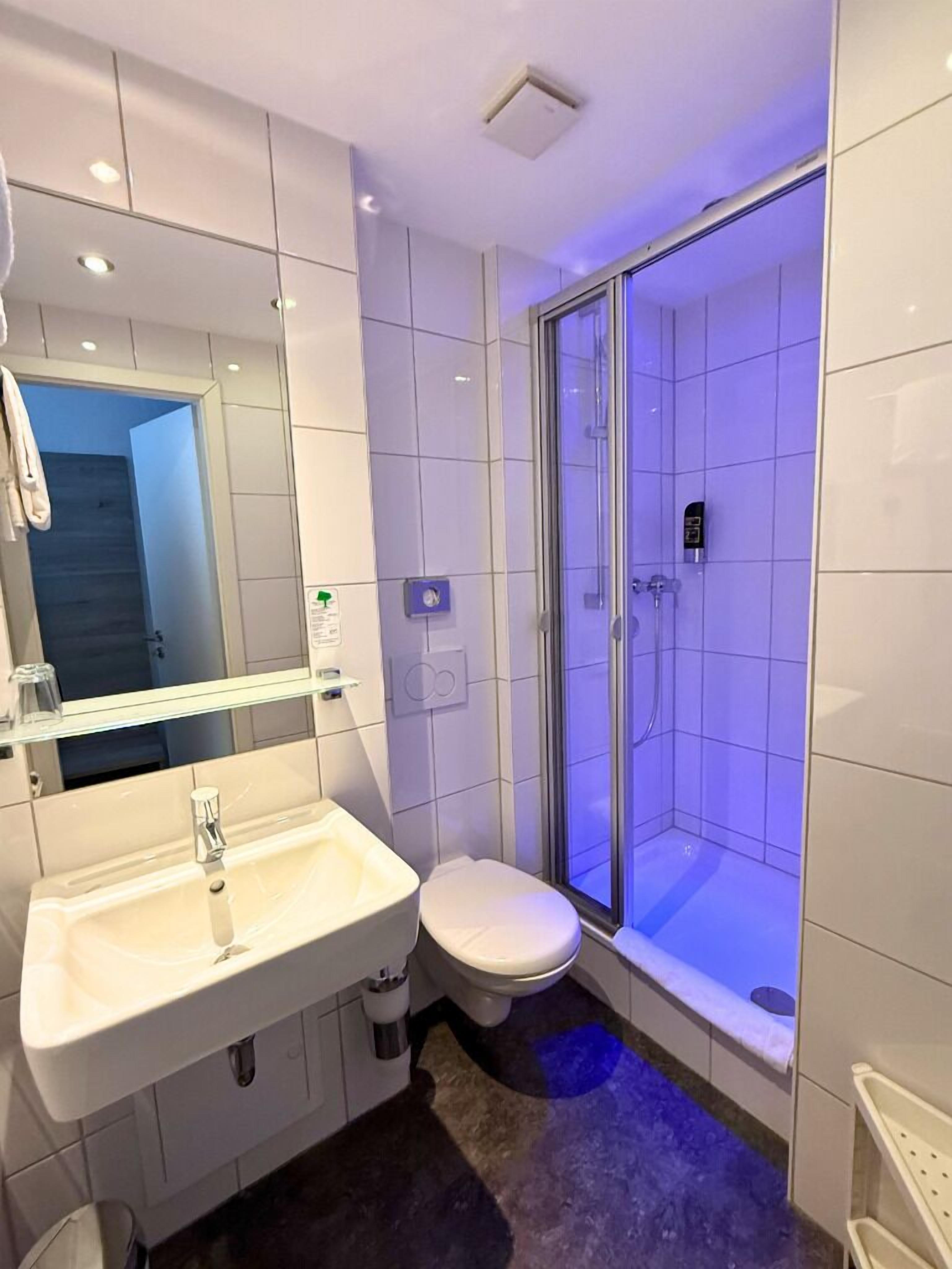 A modern bathroom with a white sink, toilet, and shower area.