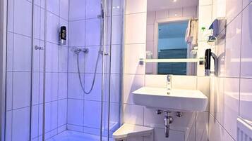 Un baño moderno con ducha envuelta en vidrio, un lavamanos blanco y un tocador pequeño.