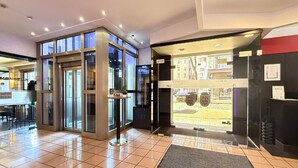 Un hall de hotel con mostrador de recepción, puerta de cristal de acceso y vista a la calle.