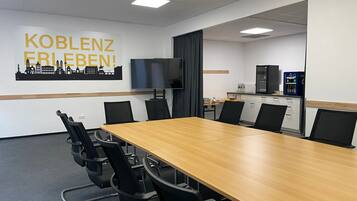 A conference room with a long table, black chairs, a TV, a kitchenette, and a cityscape poster on the wall.