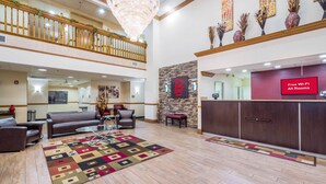 A hotel lobby with a reception desk, a seating area with sofas, a patterned rug, and a chandelier.