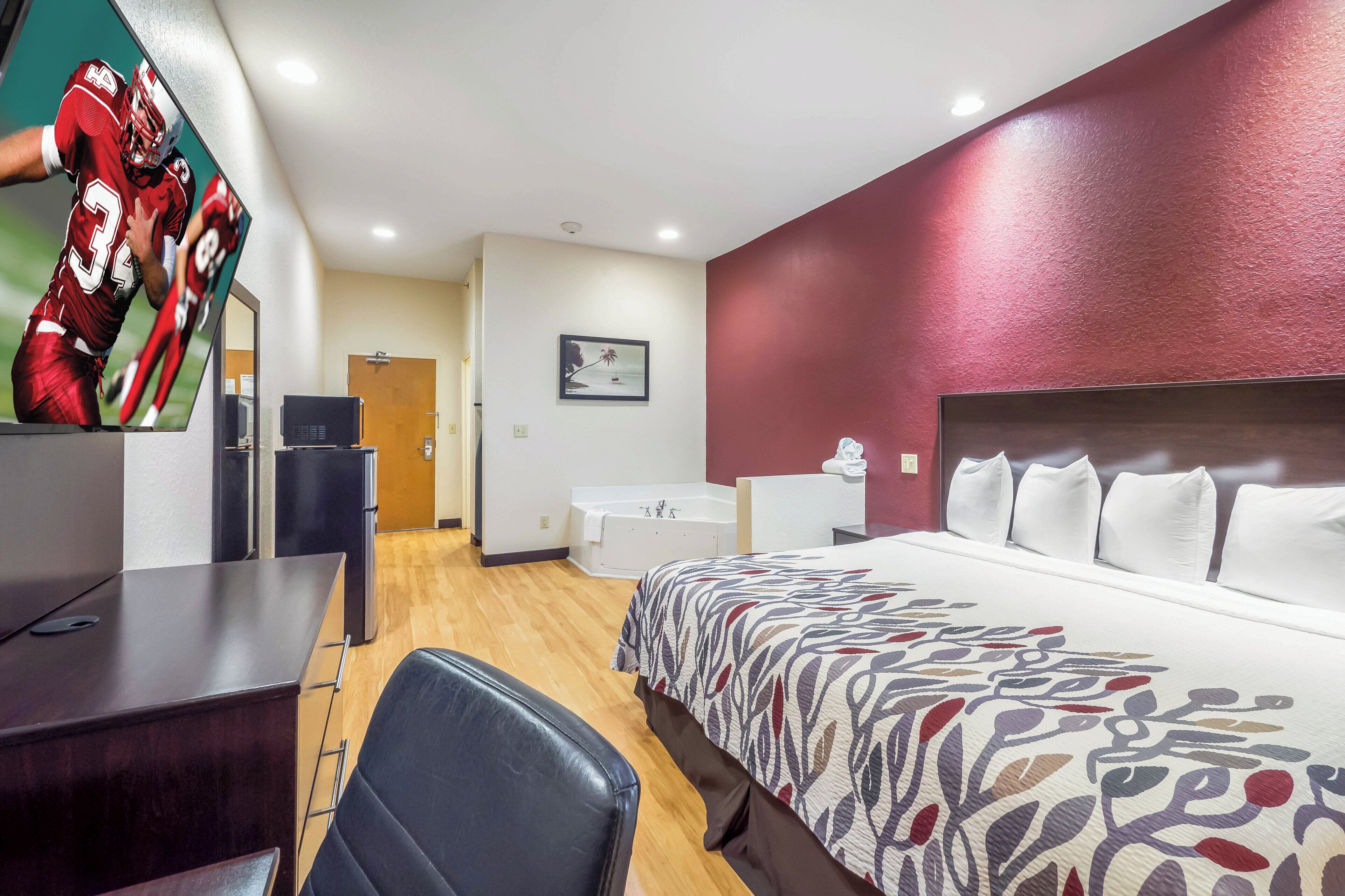A hotel room with a bed, a desk, a chair, a television, a bathroom, and a door.