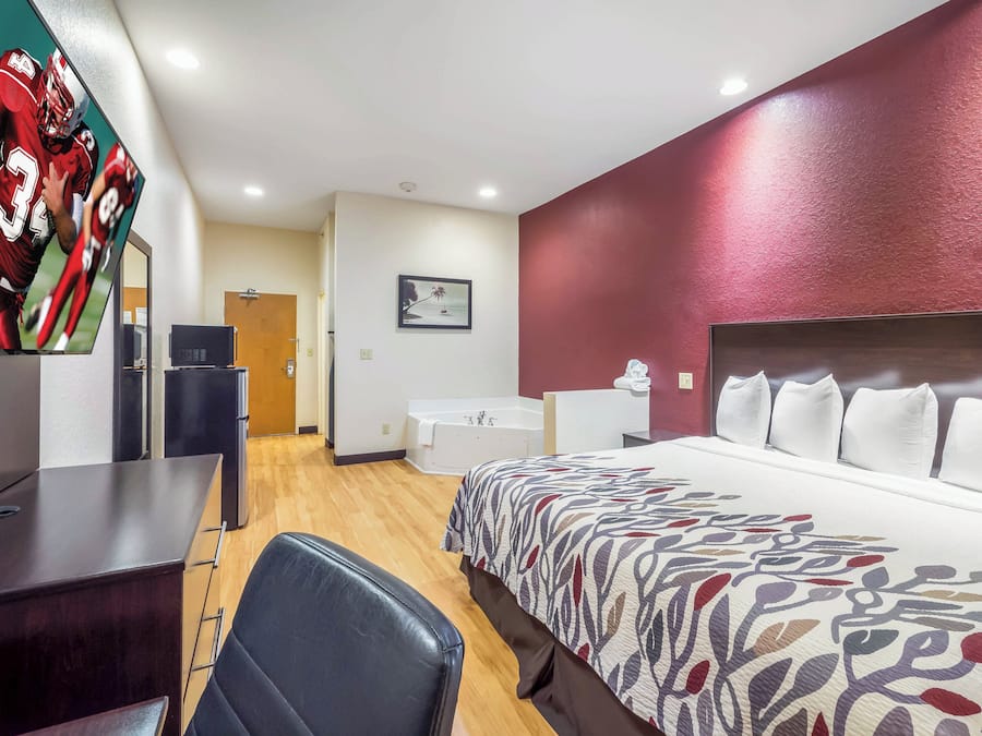 A hotel room with a bed, a desk, a chair, a television, a bathroom, and a door.