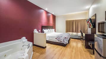 Ein Hotelzimmer mit einem großen Bett, einer separaten Sitzecke, einem Flachbildfernseher, einer Minibar und einem Badezimmer mit Badewanne und Waschbecken.