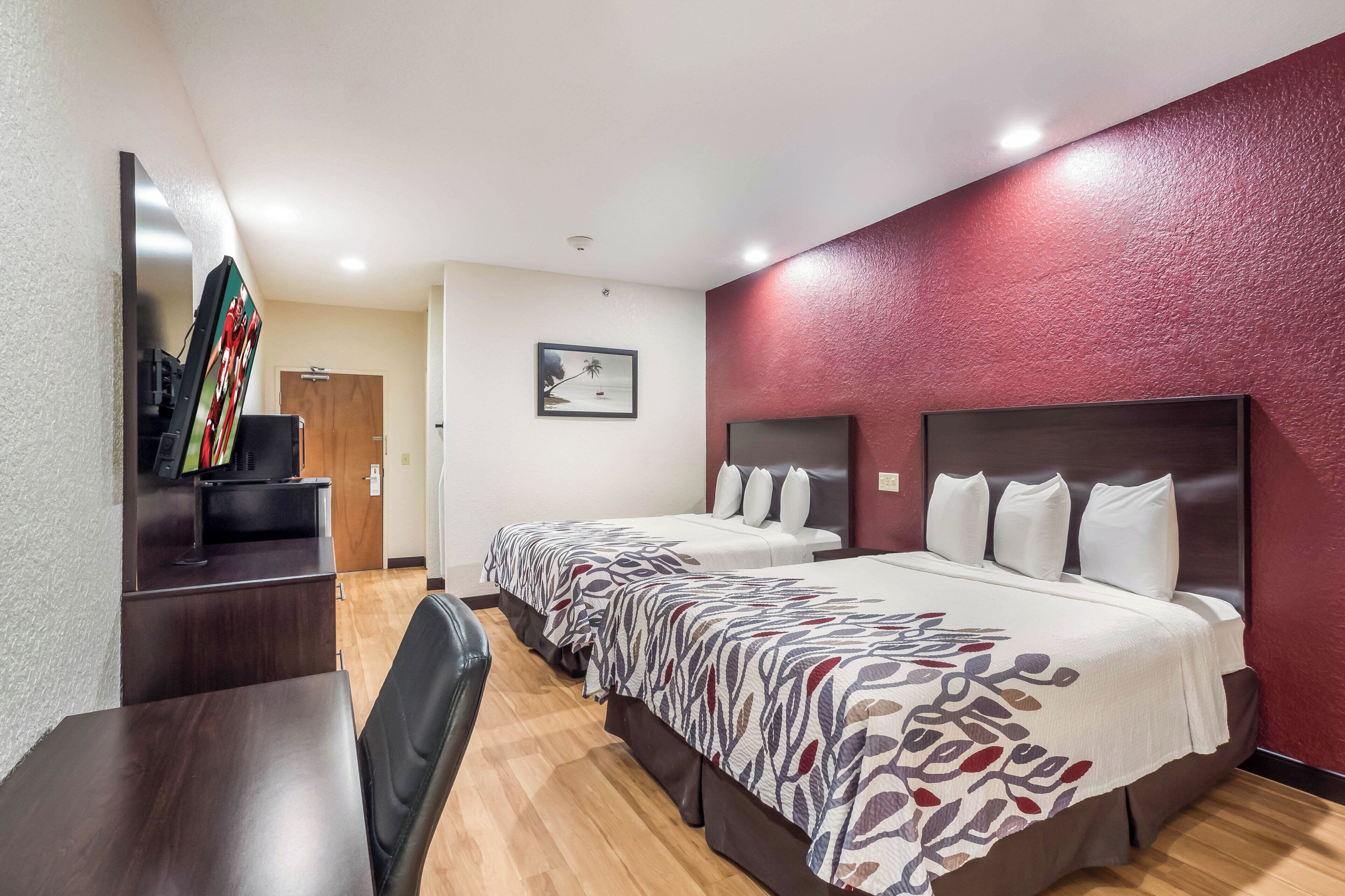 Ein Hotelzimmer mit zwei Betten, einem Schreibtisch, einem Fernseher und einer roten Wand mit Struktur.