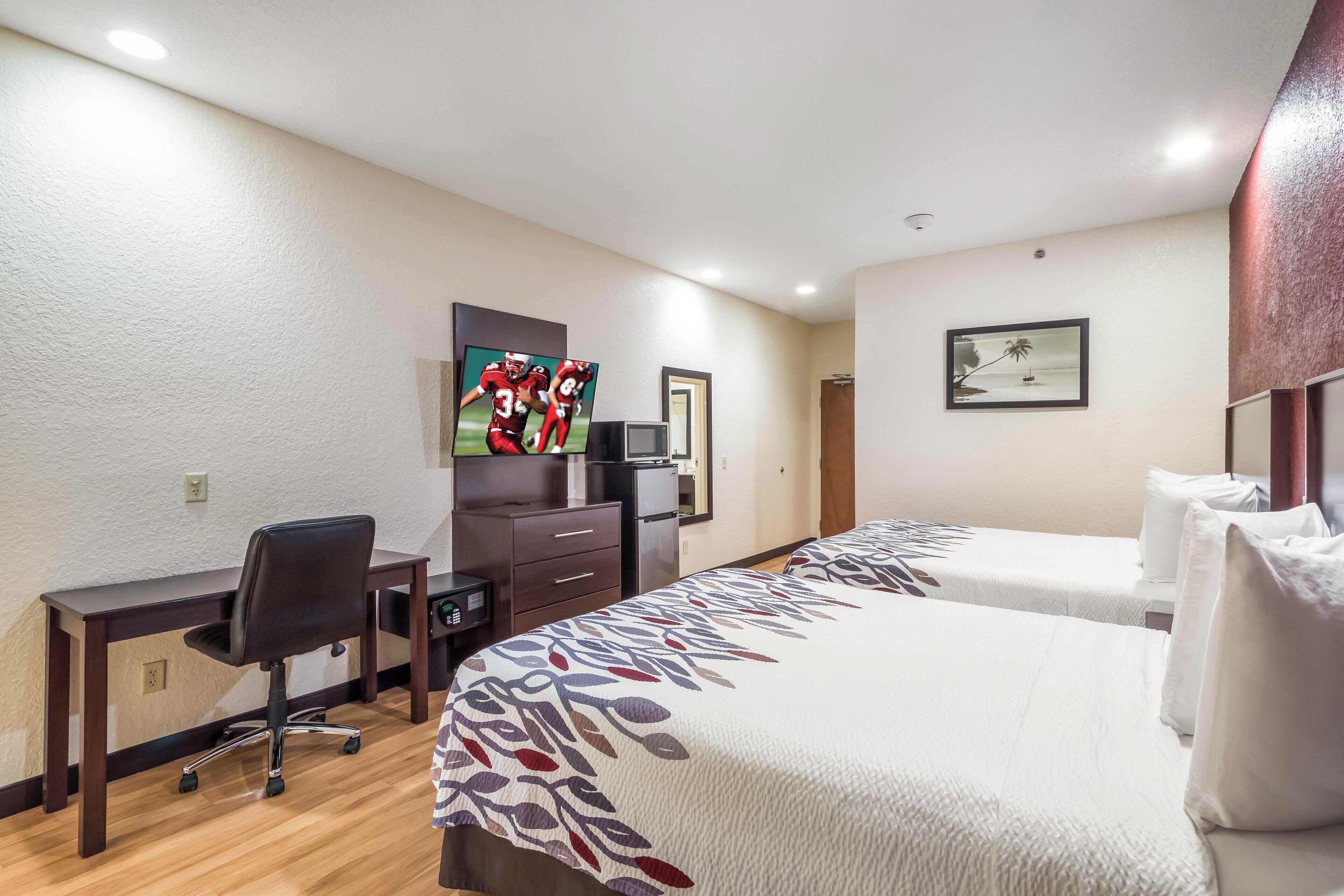 Ein Hotelzimmer mit Schreibtisch, Stuhl, zwei Betten, einem Fernseher und Kunstwerken an den Wänden.