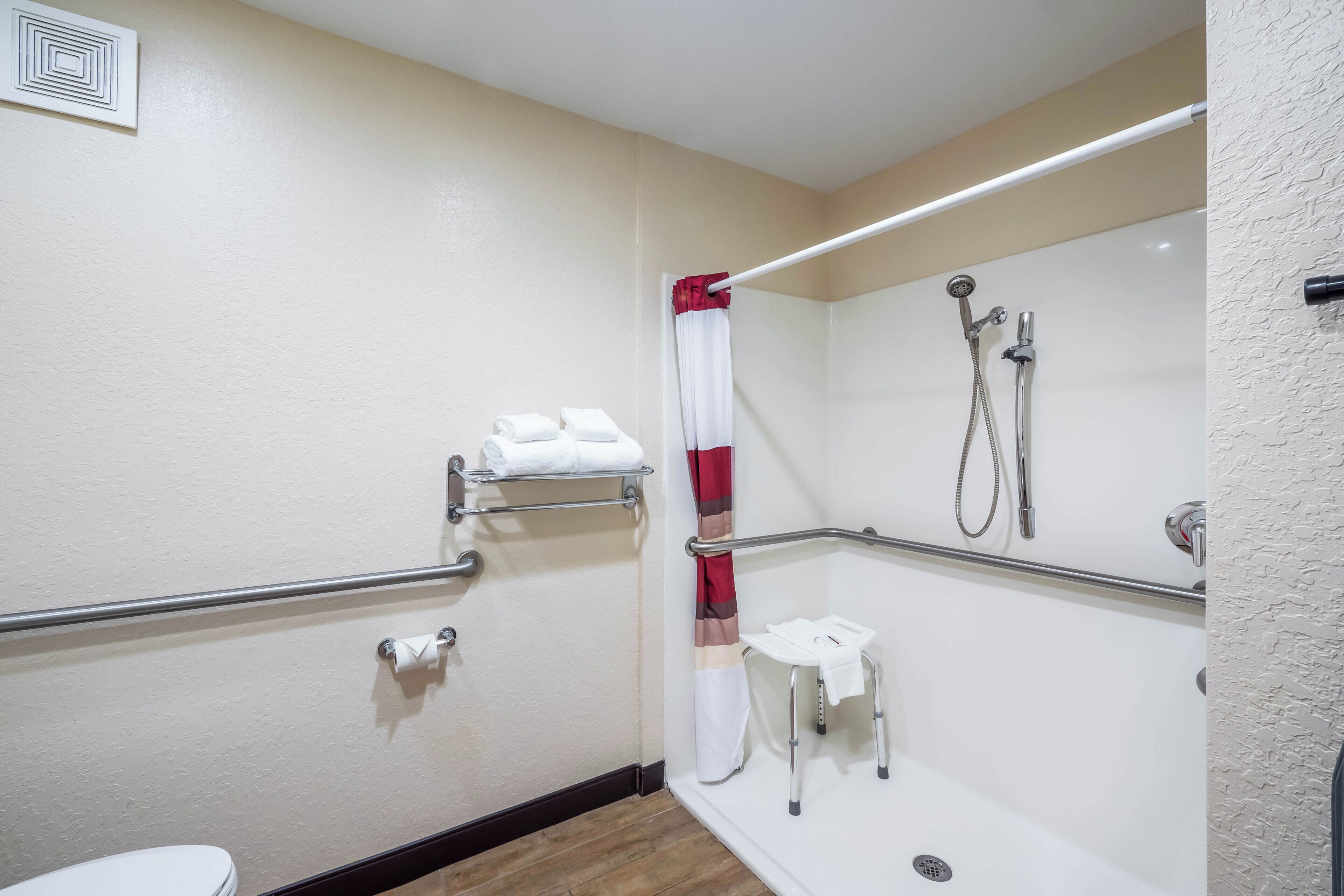 A bathroom with a shower, grab bars, a toilet, and a towel rack.