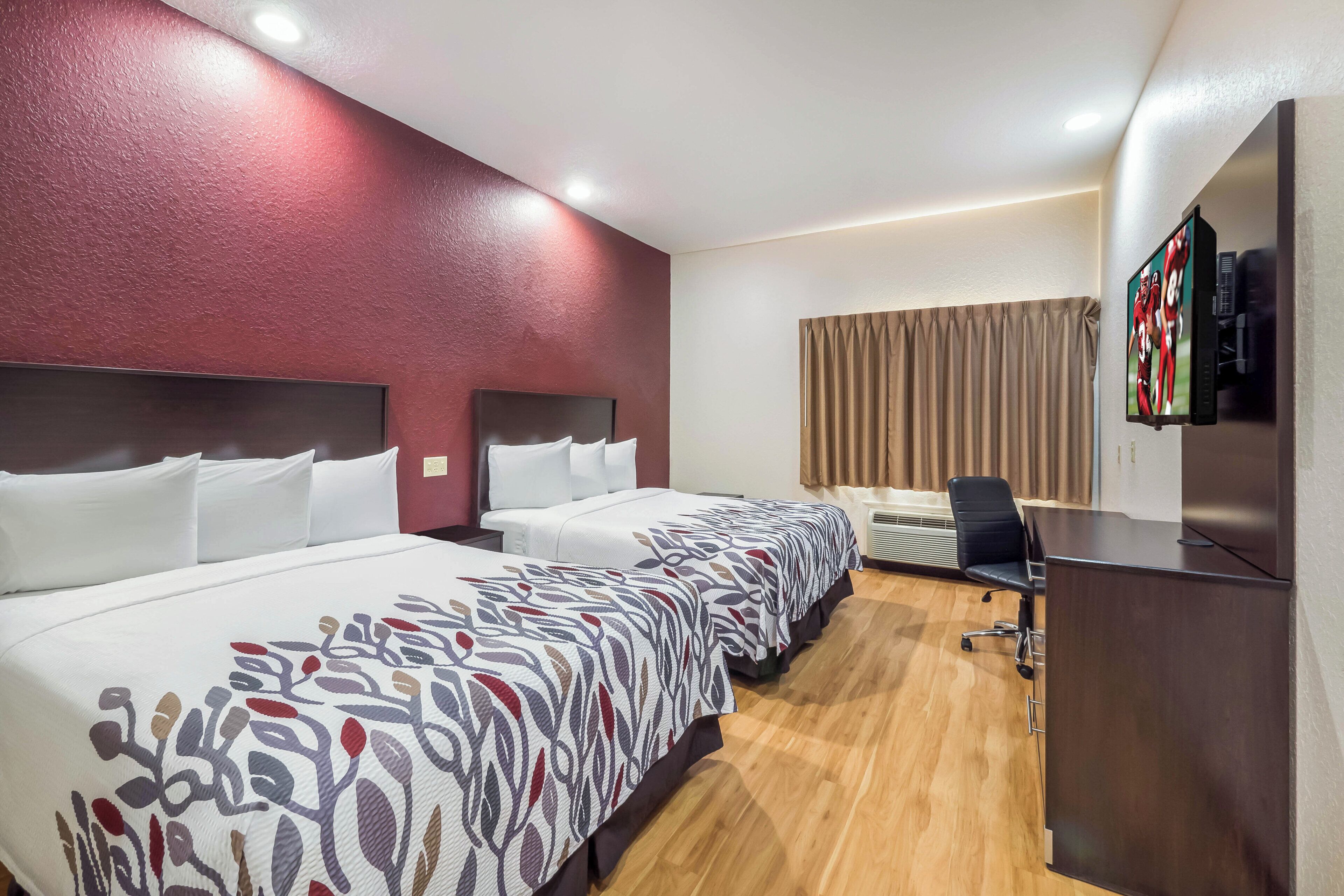 Une chambre d’hôtel avec deux lits, un bureau, une chaise, une télévision et une fenêtre avec des rideaux.
