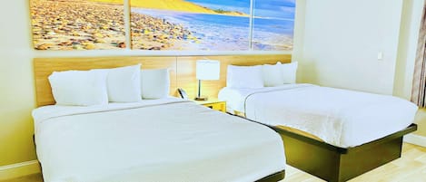 Habitación de hotel con dos camas, un gran mural de playa en la pared y piso de madera.