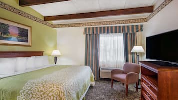 Une chambre d’hôtel avec un grand lit, deux chaises, une télévision et une fenêtre avec des rideaux.