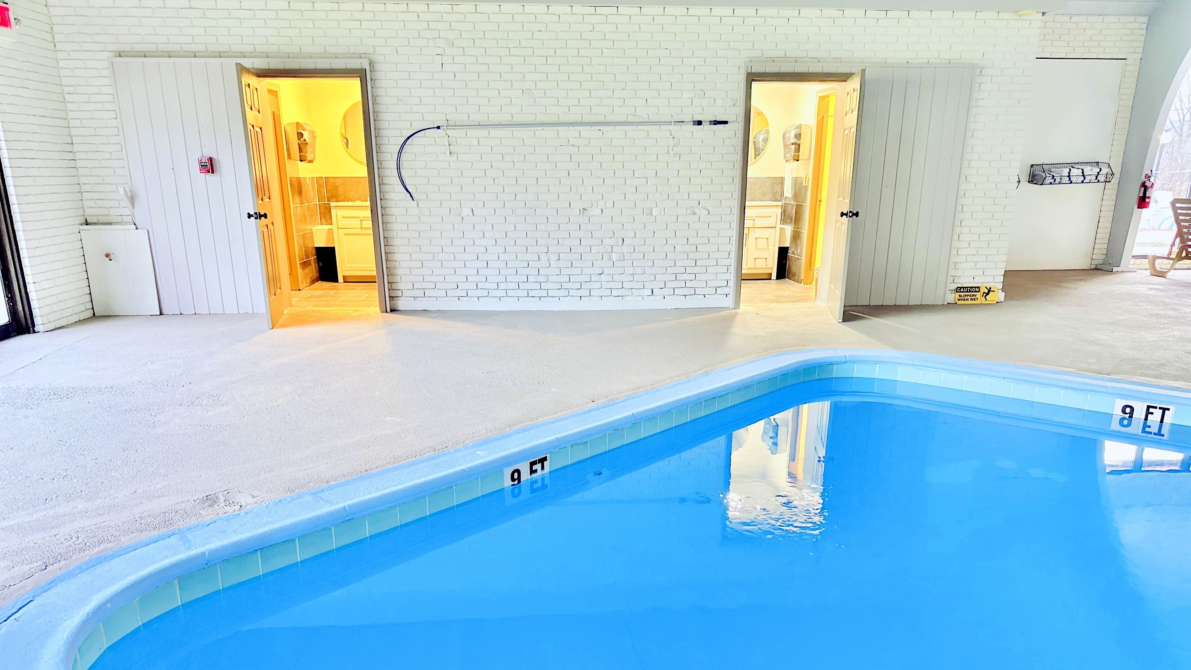 A swimming pool with a white brick wall and two doors leading to a bathroom.