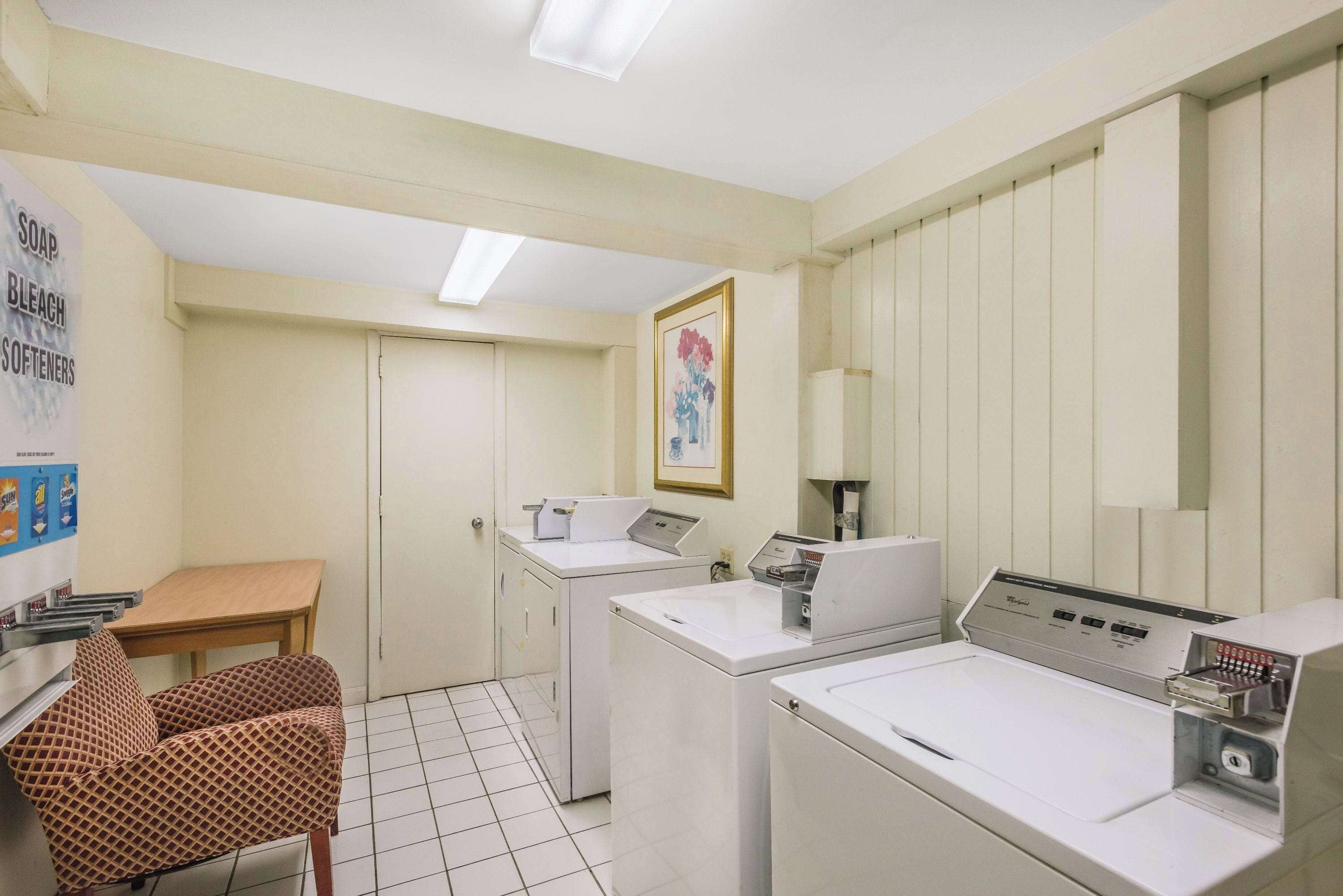 A laundry room with two washing machines, a table, and a chair.