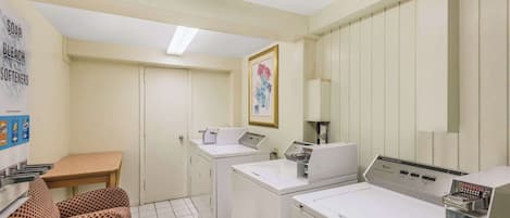 A laundry room with two washing machines, a table, and a chair.