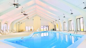 Ein Innenpool mit hoher Decke, mehreren Deckenventilatoren und einem Sitzbereich mit Stühlen und Tischen.