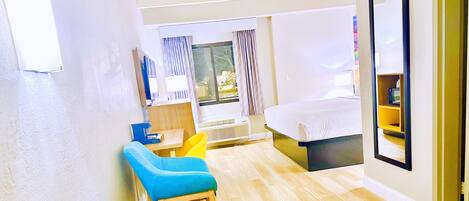 A hotel room with a bed, a desk, a chair, a window with curtains, and a wall-mounted mirror.