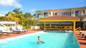 A swimming pool with lounge chairs and a covered area, surrounded by a building with balconies. - Bird Rock Beach Hotel (Basseterre)