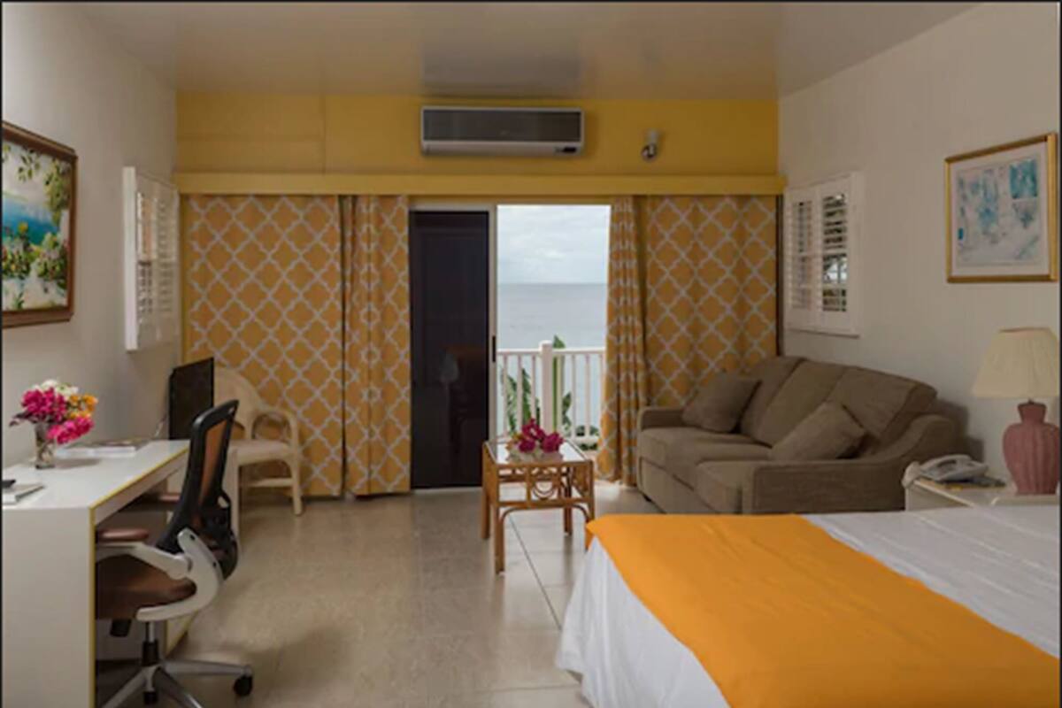A hotel room with a bed, a desk, a chair, a sofa, and a balcony with a view of the sea.