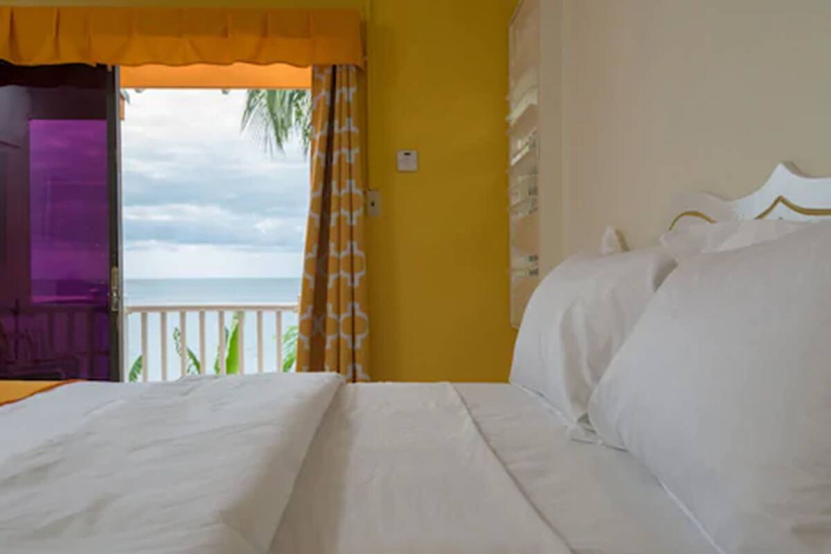 A hotel room with a bed, a view of the ocean, and a balcony with a railing.