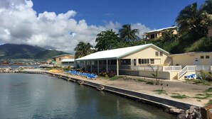 A coastal hotel with a white building, a pool with blue lounge chairs, and a view of the sea and mountains. - Bird Rock Beach Hotel (Basseterre)