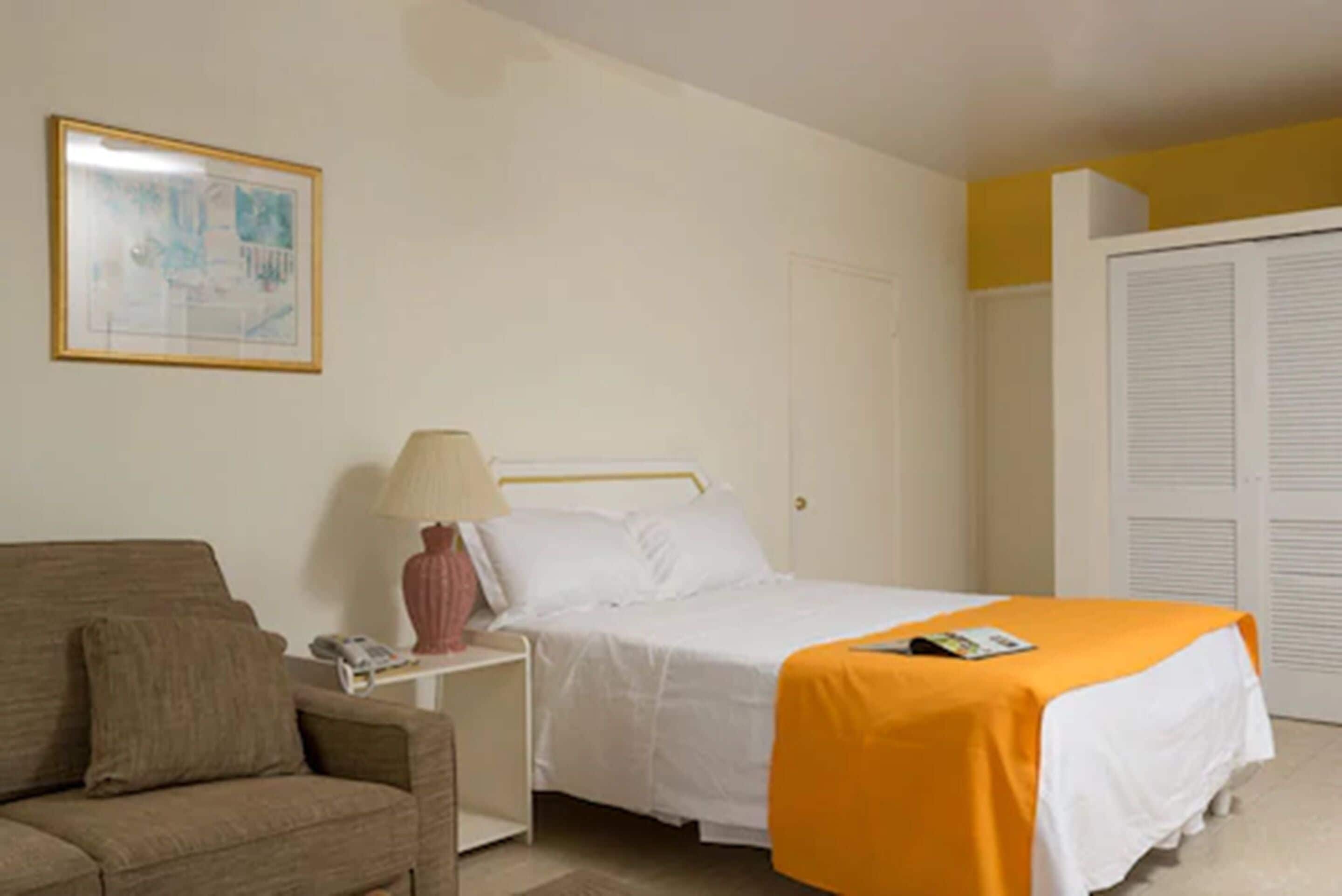 A bedroom with a bed, a nightstand, a lamp, a couch, and a door with latches.