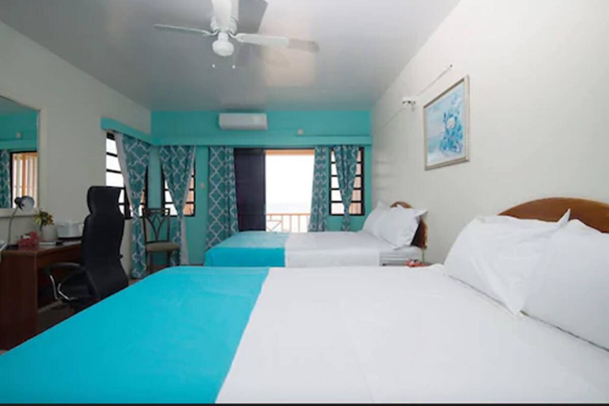 A hotel room with two beds, a desk, a chair, and a ceiling fan.