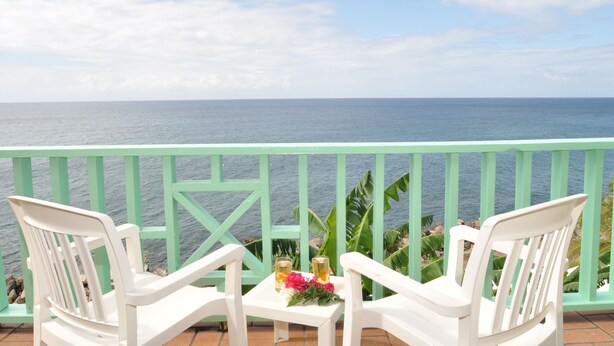 A balcony with two white chairs and a small table with drinks and flowers, overlooking a calm sea. - Bird Rock Beach Hotel (Basseterre)