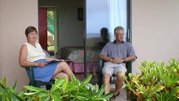 Dos personas sentadas en un balcón con vista a un edificio y un jardín.