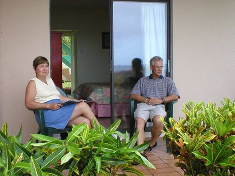 Dos personas sentadas en un balcón con vista a un edificio y un jardín.