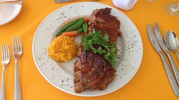 A plate with a meat dish, vegetables, and mashed potatoes on a table with a yellow tablecloth.