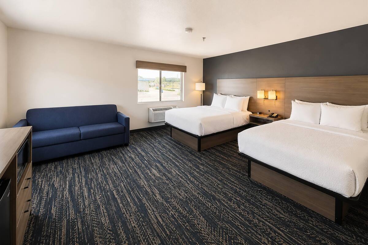 A hotel room with two beds, a sofa, a desk, a lamp, and a window.