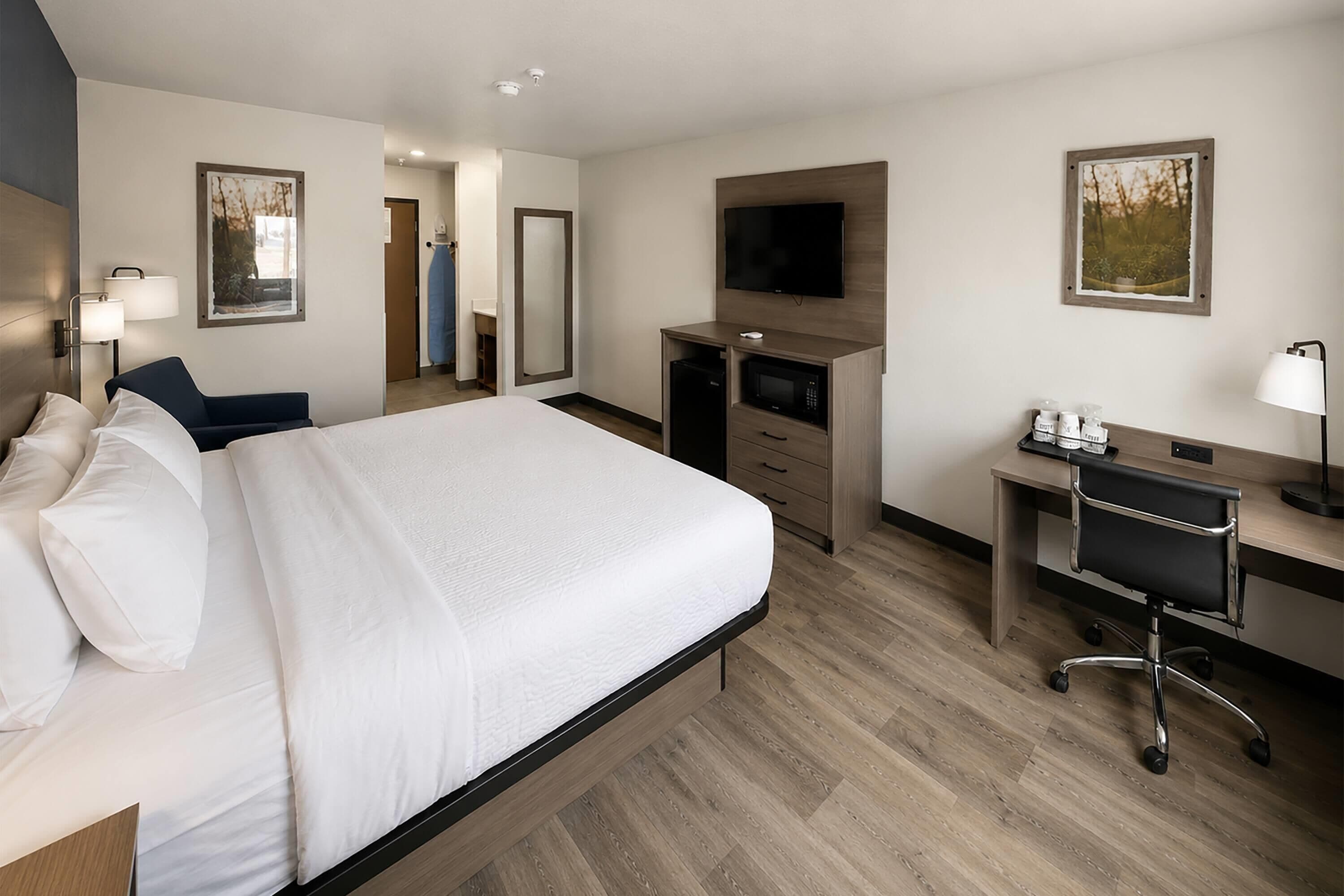 Ein Hotelzimmer mit Bett, Schreibtisch, Stuhl, Fernseher und Spiegel.
