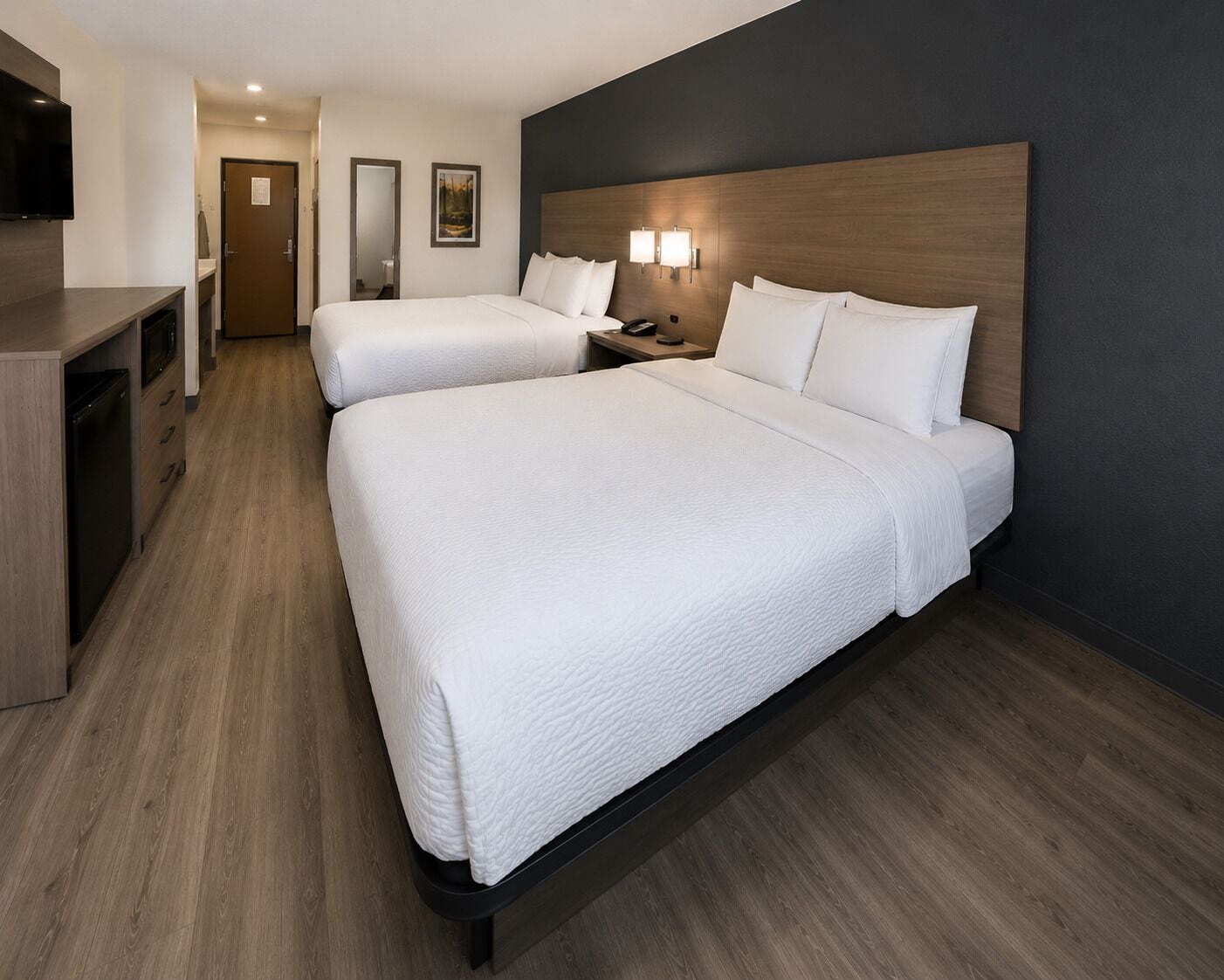 A hotel room with two beds, a desk, a TV, and a nightstand with lamps.