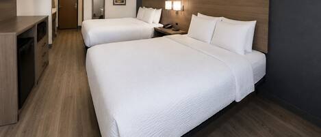 A hotel room with two beds, a desk, a TV, and a nightstand with lamps.