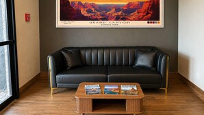 Un sofá de cuero negro, una mesa de centro de madera con revistas, y un cartel enmarcado del Gran Cañón en la pared.