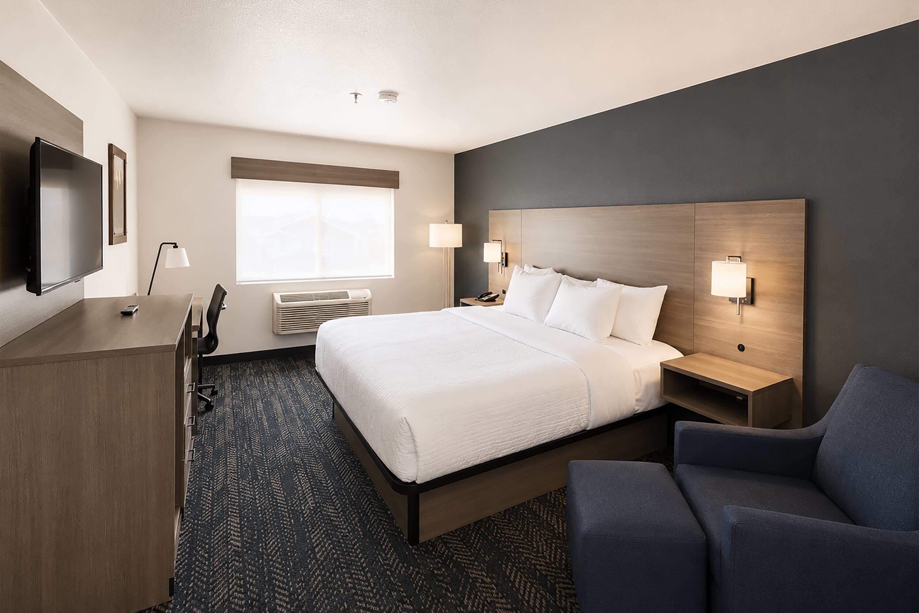A hotel room with a bed, bedside tables, a desk, a TV, and a chair.