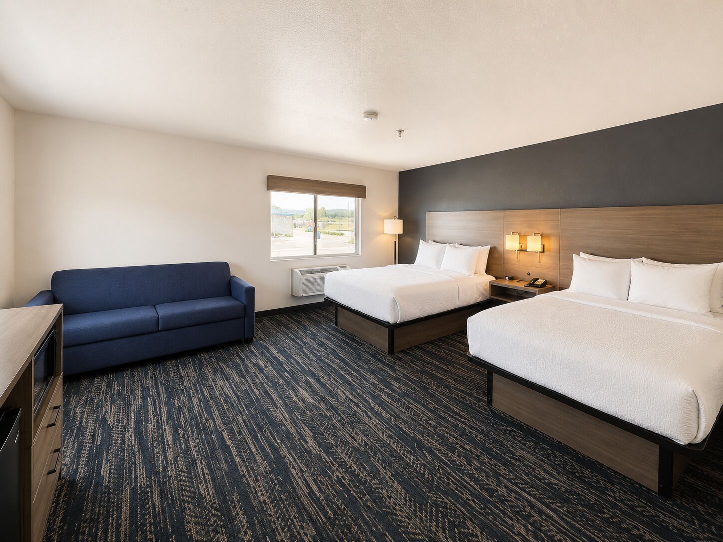 Quarto de hotel com duas camas, um sofá, uma escrivaninha e uma janela com vista.