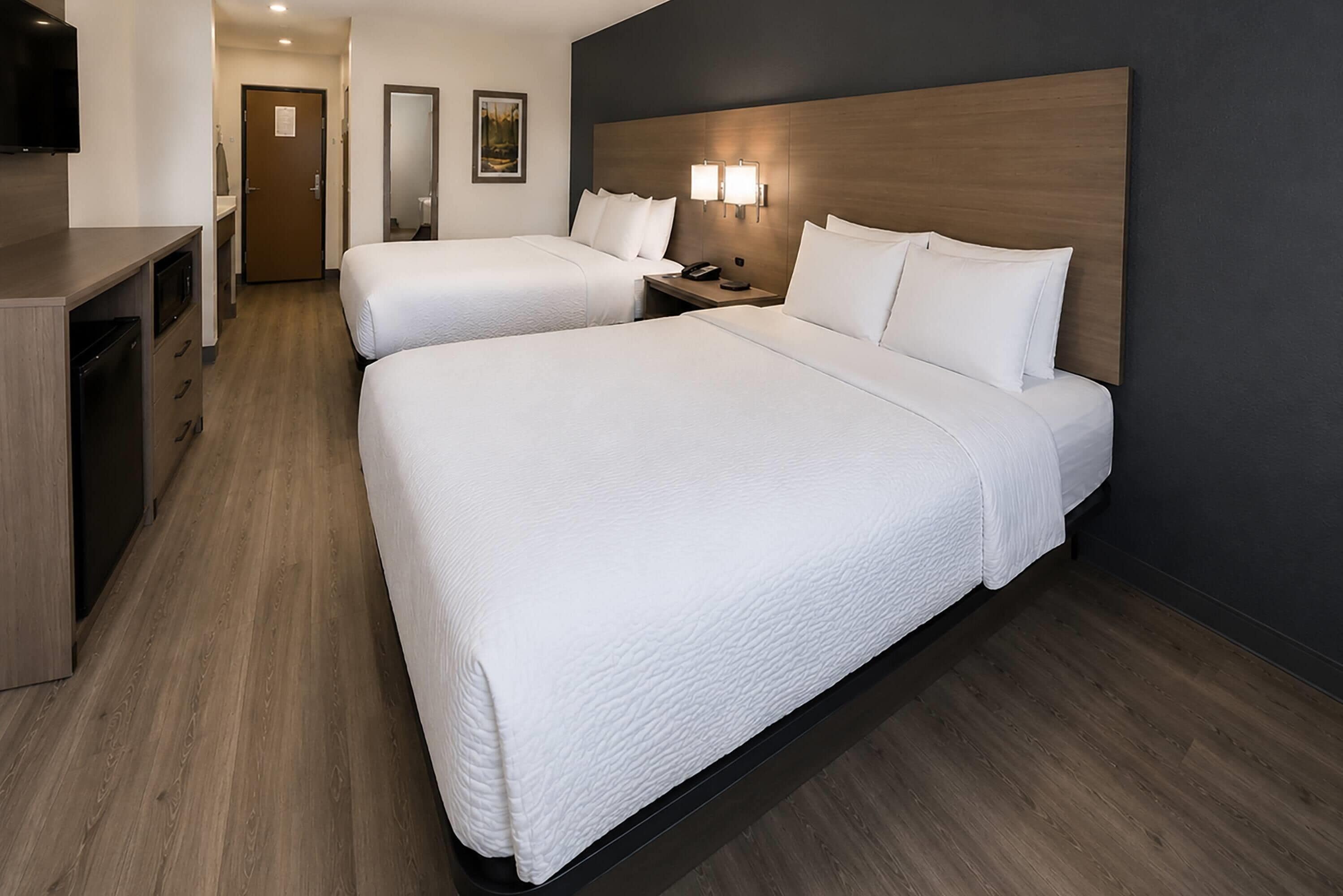 A hotel room with two beds, a desk, a mirror, and a television.