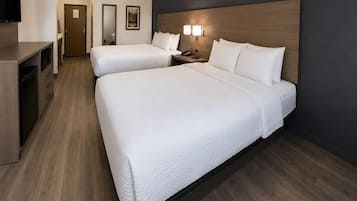 A hotel room with two beds, a desk, a mirror, and a television.