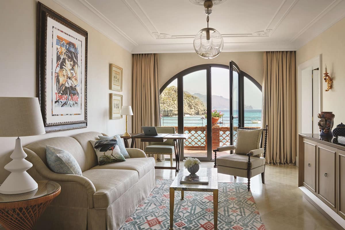 Un salon comprenant un canapé, des fauteuils, une table basse, un ordinateur portable et une vue sur la mer, visible à travers une grande fenêtre en arc de cercle.