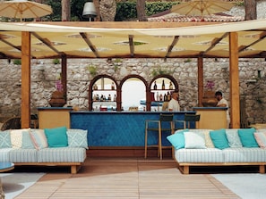A bar area with a stone wall backdrop, wooden furniture, and a seating arrangement with cushions.