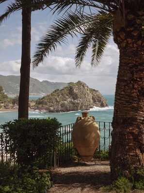 A coastal view with a large vase, palm trees, and a rocky island in the background. - Villa Sant'Andrea, A Belmond Hotel, Taormina Mare (Taormina)