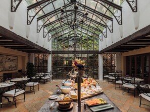 A spacious indoor area with a glass ceiling, multiple dining tables, and a central buffet with various food items.