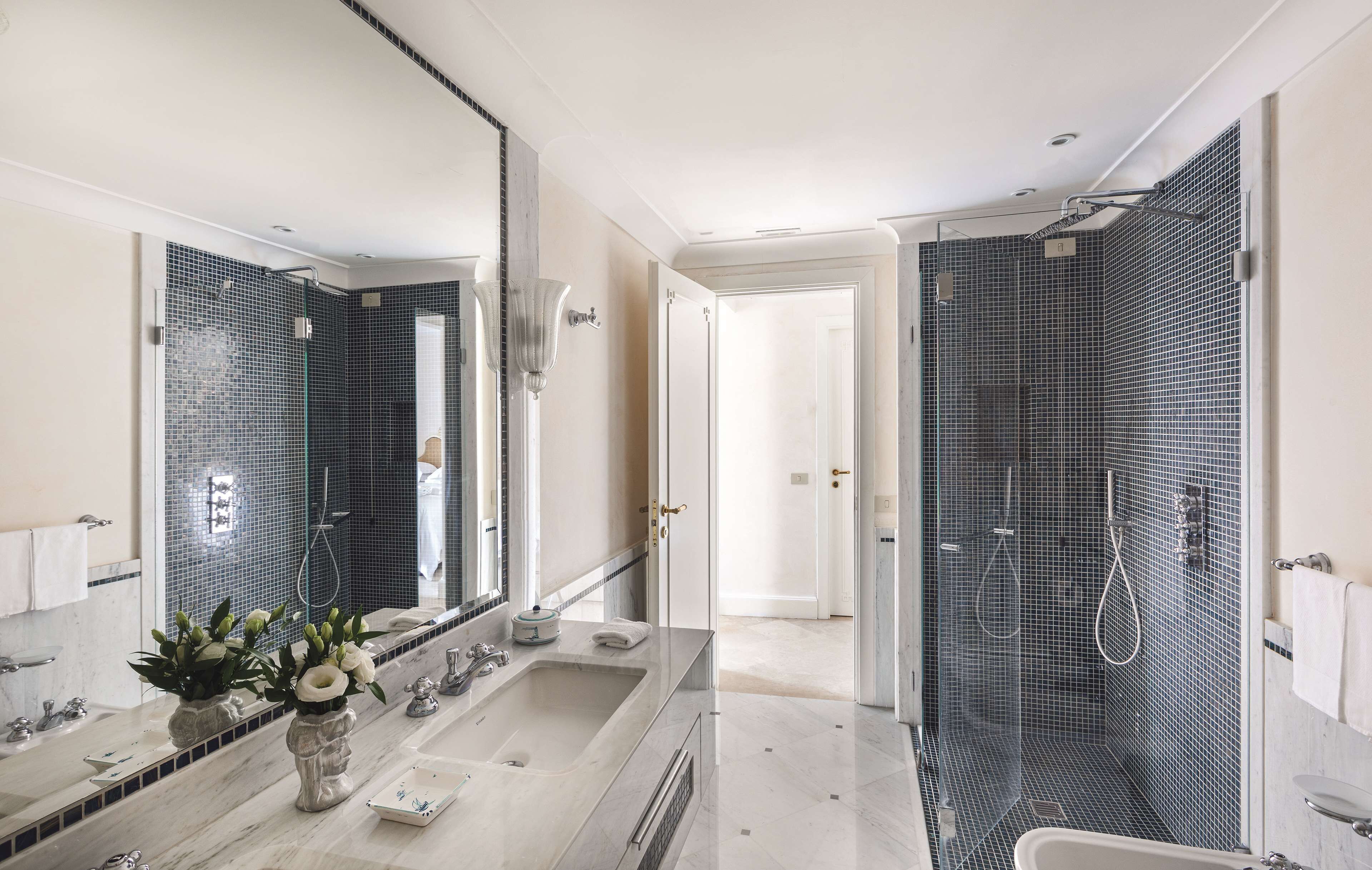 A modern bathroom with a large mirror, two sinks, a shower, and a toilet.