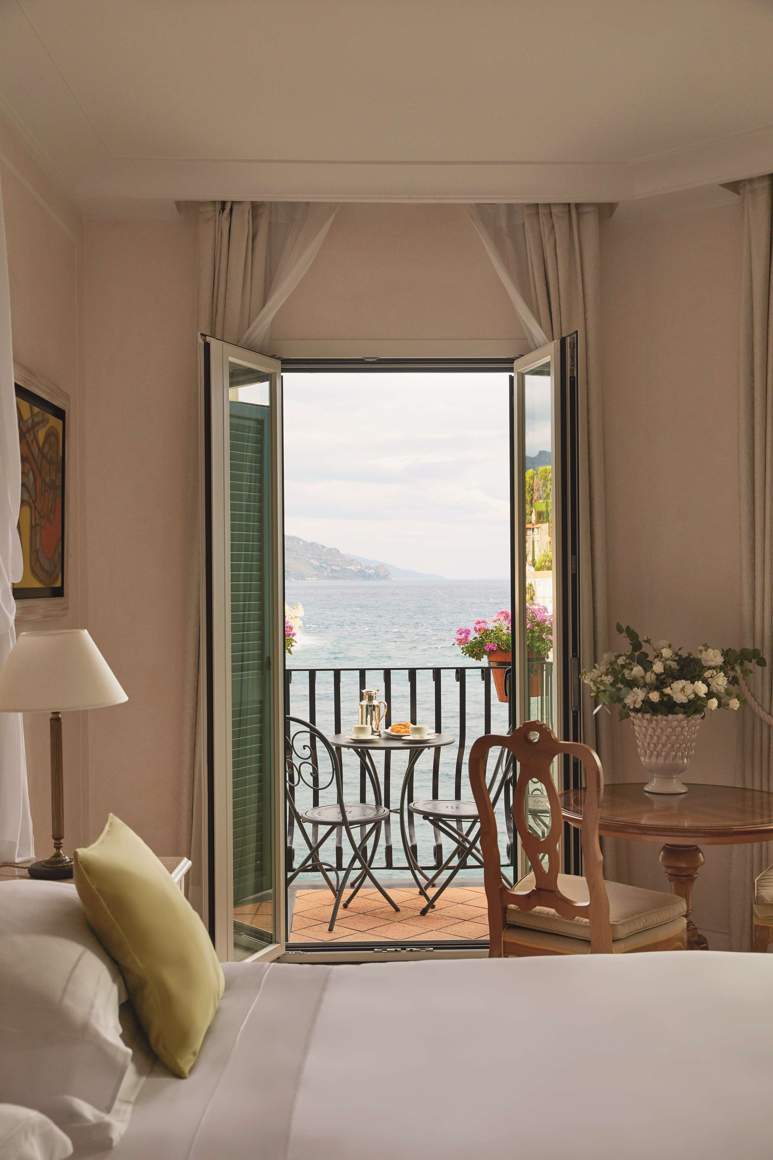 Une chambre d’hôtel avec un lit, une chaise, une table, une lampe et une vue sur la mer.