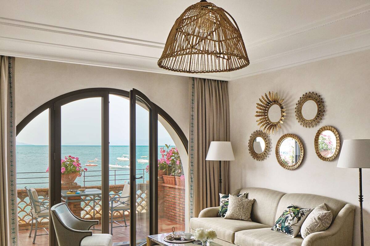 Un salon spacieux comprenant un canapé, des fauteuils et une table basse. Une grande fenêtre offre une vue sur la mer.