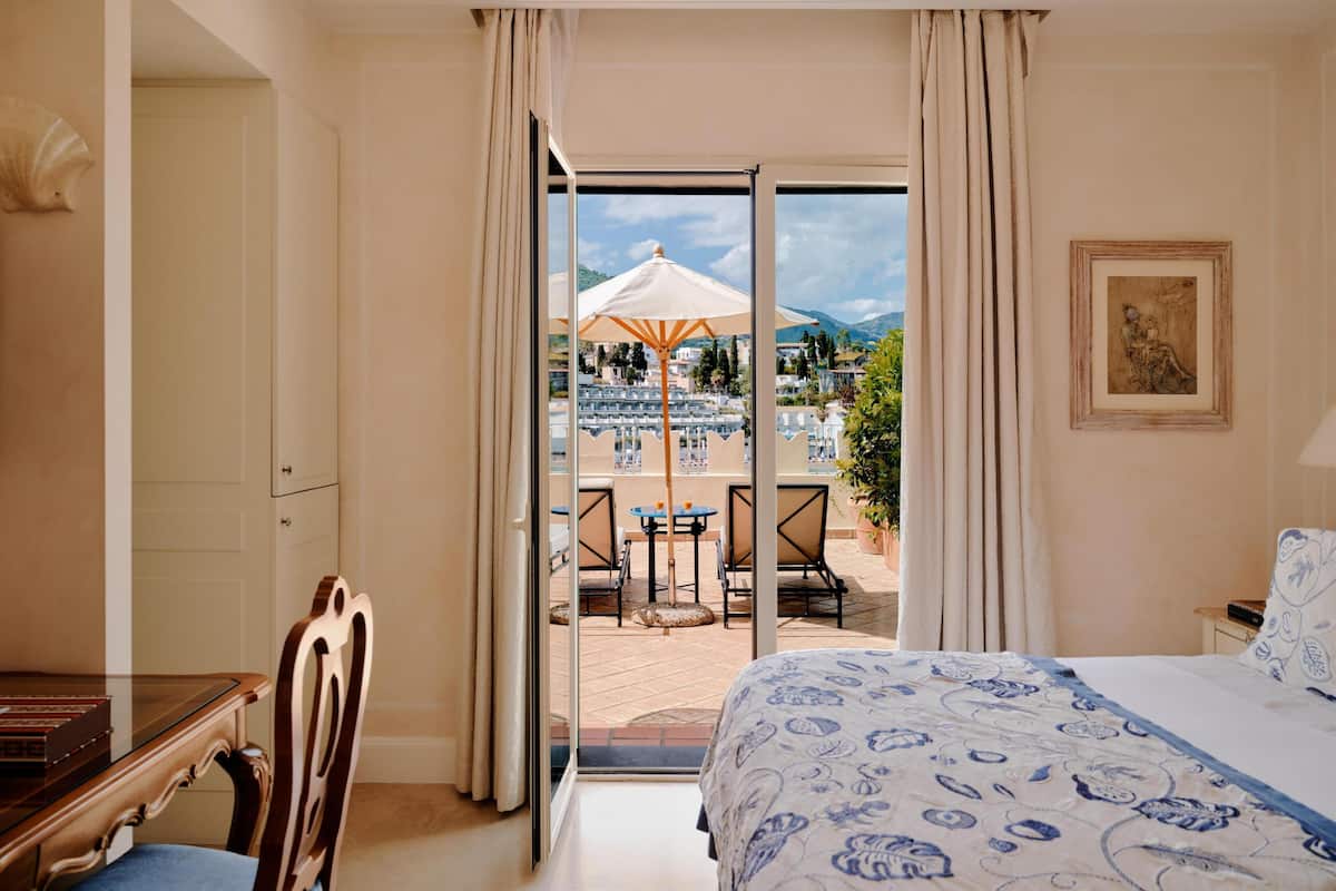 Une chambre d’hôtel comprenant un lit, un bureau, une chaise, un balcon avec mobilier d’extérieur et une vue sur le paysage.