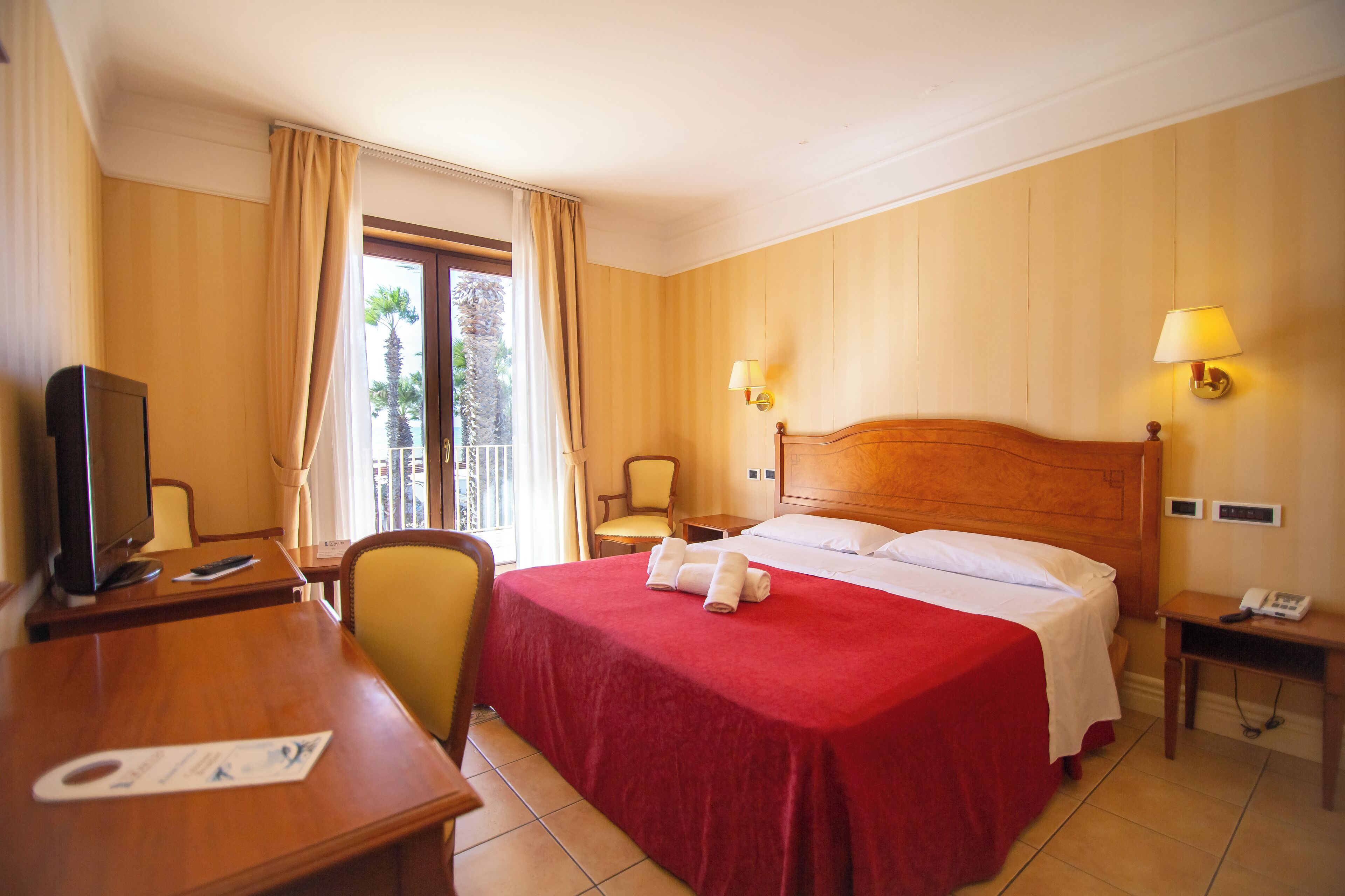 A hotel room with a bed, a desk, a chair, a television, and a window with curtains.