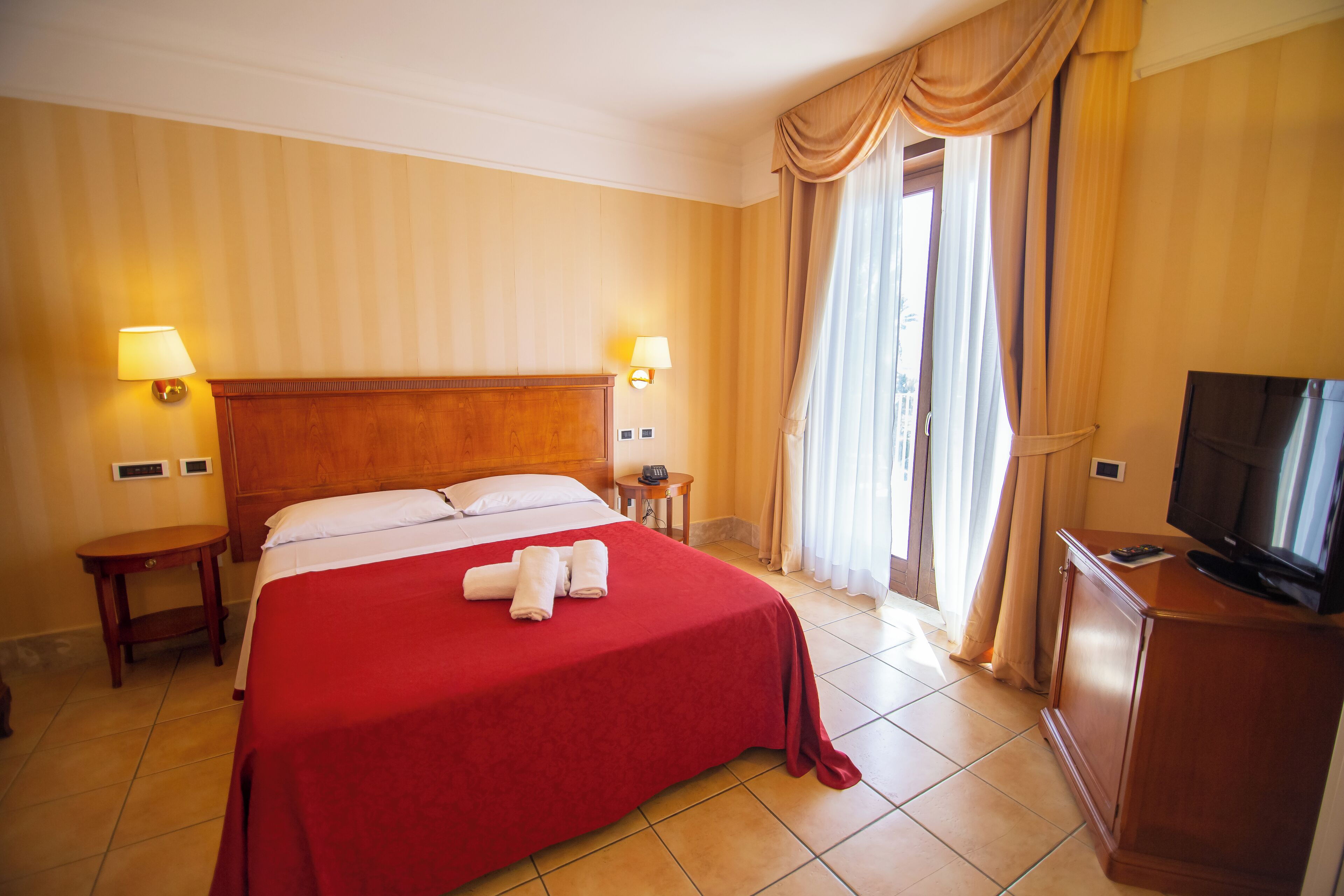 Habitación de hotel con una cama grande, dos lámparas de noche, un televisor y vistas a la ciudad por la ventana.