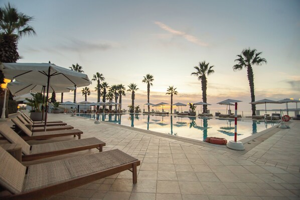 A poolside area with lounge chairs and umbrellas, surrounded by palm trees. - Dioscuri Bay Palace Hotel (Agrigento)