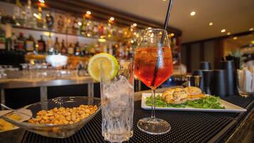 A bar setting with a glass of iced drink, a bowl of nuts, and a plate of food.